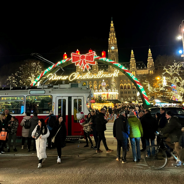 Bright neon lights from an entrance to the Vienna Christmas Market as the crowd gathers.